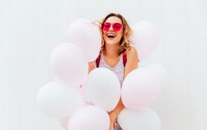 junge frau mit roter sonnenbrille am lachen und hält luftballons in der hand